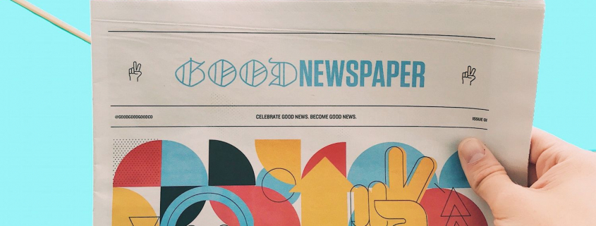 Eine Hand hält eine Zeitung mit der Überschrift Good News vor blauem Hintergrund