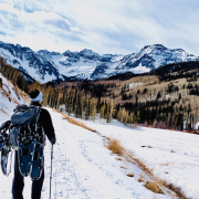 Ein Mensch mit Schneeschuhen am Rucksack wandert durch winterliche Landschaft